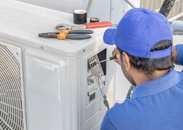 Blue-uniformed technician repairing the service panel of an outdoor air conditioner