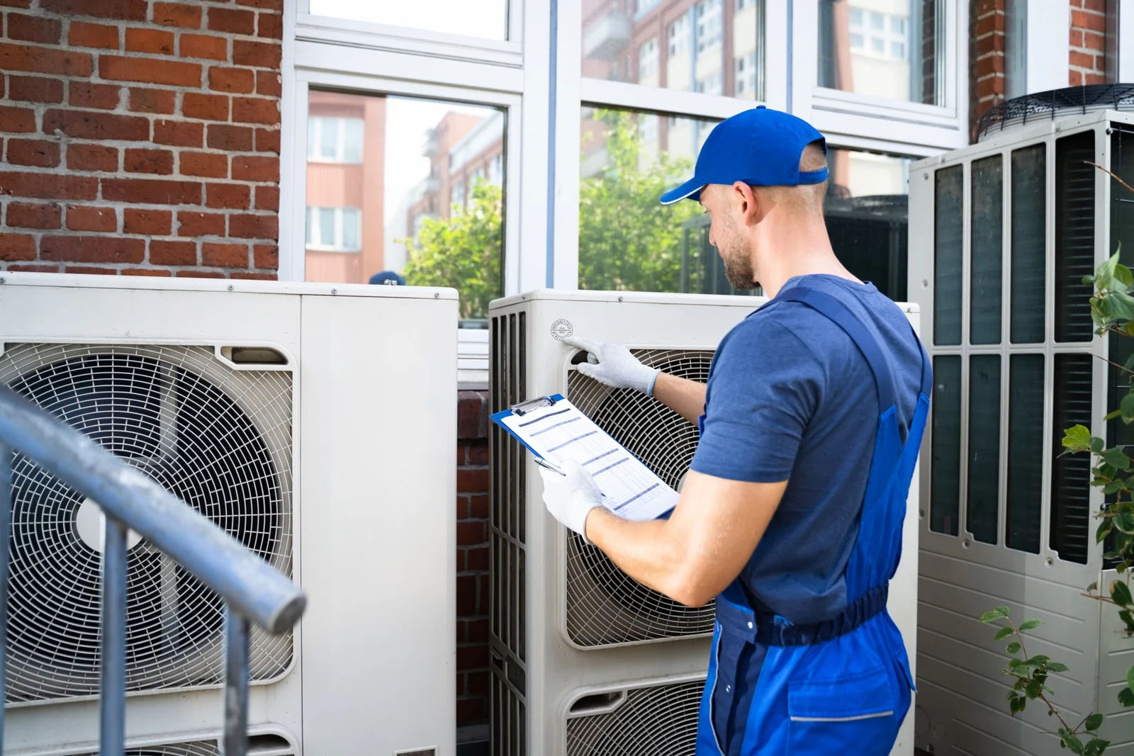 Technician inspecting outdoor air-conditioning units and recording readings on a clipboard